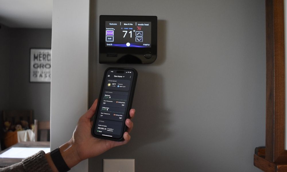wifi thermostat Image of a homeowner verifying that their new wifi thermostat and smartphone app are in sync.