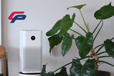 A room air purifier sitting on a small table next to a healthy green plant.