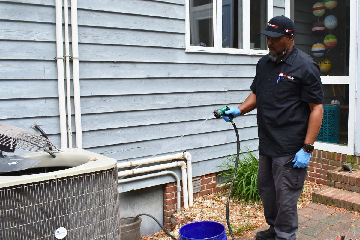 Comfort Plus HVAC Technician Mike H rinses an outdoor HVAC condenser unit near Fenwick, as part of a service plan seasonal HVAC maintenance call.