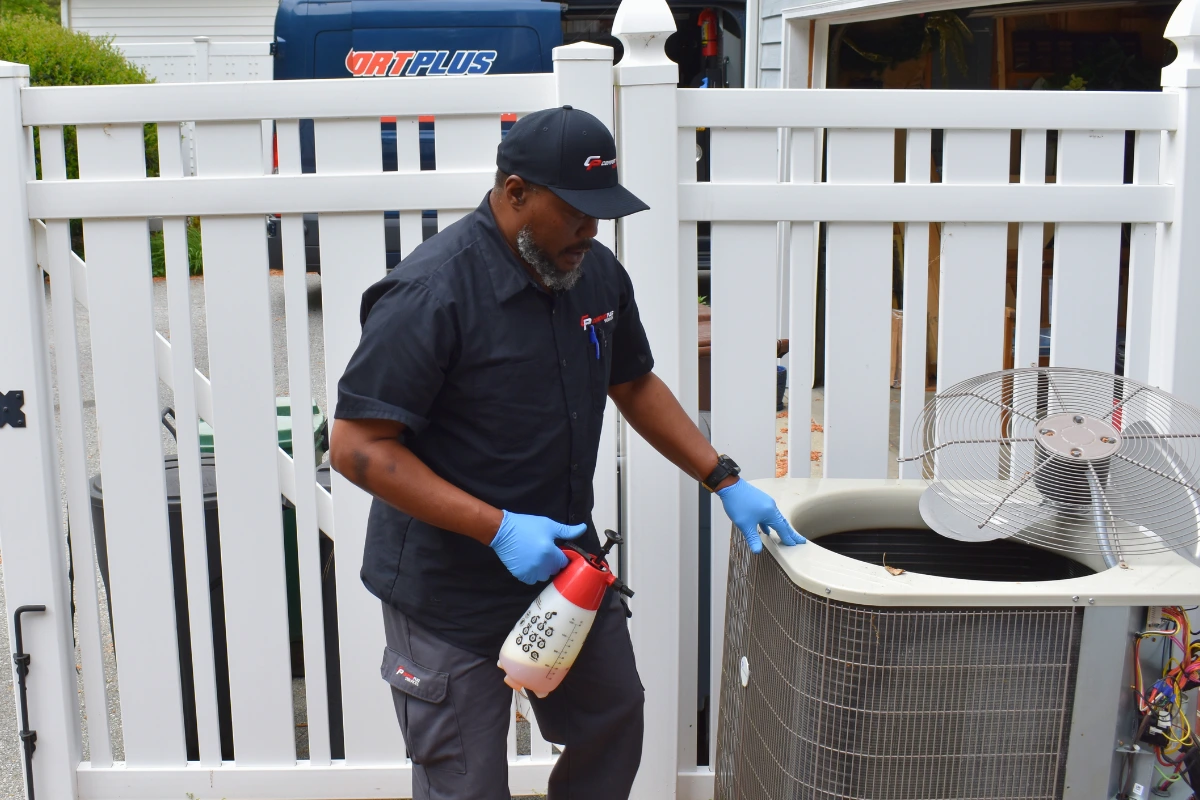 Comfort Plus HVAC Technician Mike H sprays an anti-corrosion solution on an outdoor HVAC condenser unit near Fenwick.
