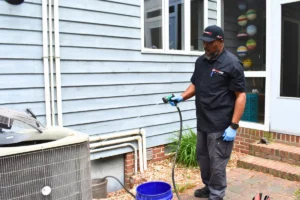 An HVAC technician cleans an outdoor condenser unit's fins of dirt and debris.